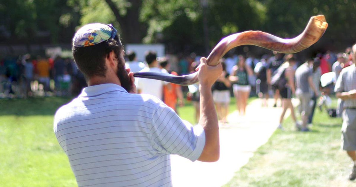 A rabbi blowing a shofar outside with his congregation