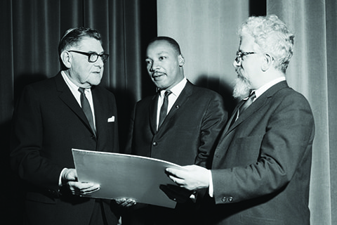 George Maislen, president of the United Synagogue of America, presents an award to Martin Luther King Jr., in November 1963. Abraham Joshua Heschel looks on.