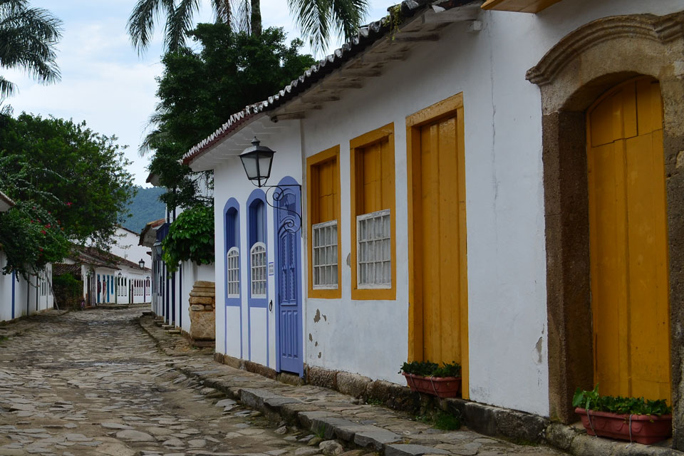 Stone road lined by white buildings painted with vibrant gold and blue doors and windows.