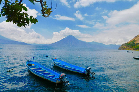 Two blue tethered boats with motors floating in a lake surrounded by mountains.