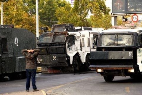 View of back of a person with hands up in surrender in front of military trucks