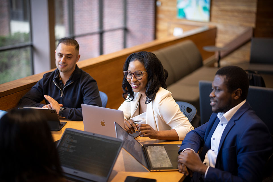 Four people with computers dressed in business attire talking and working at a table.