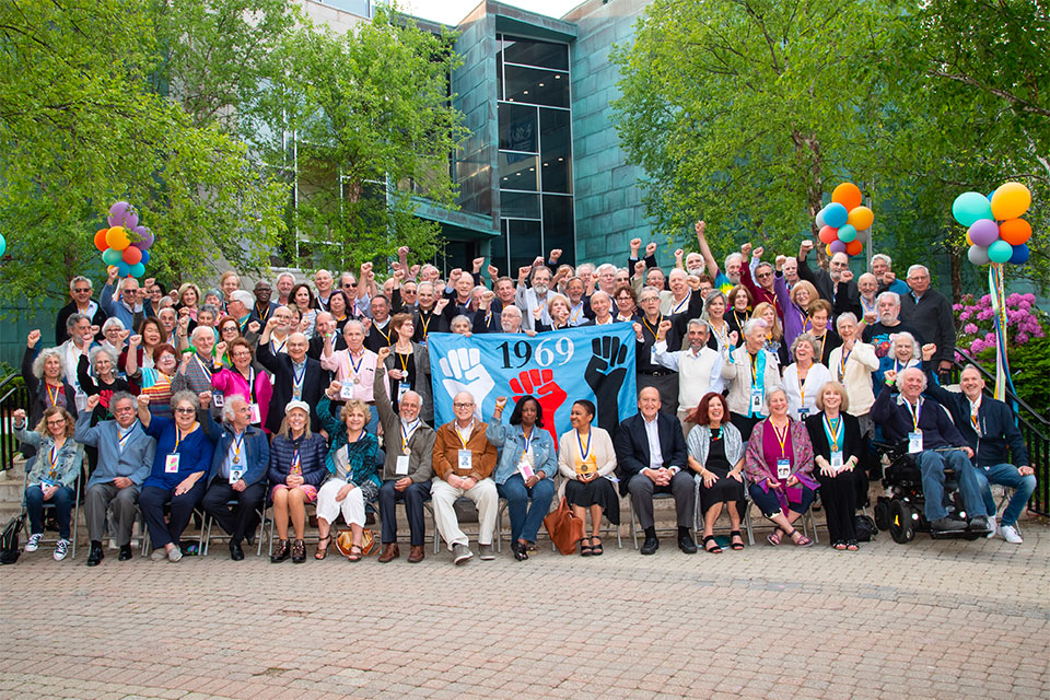 Class of 1969, some with raised fists, poses as a group at Reunion