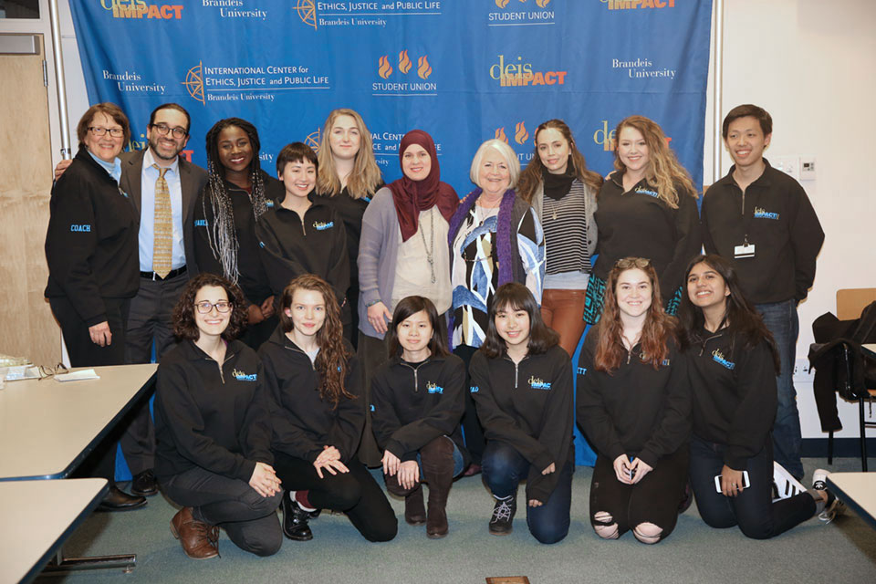 A group of students and speakers in front of the 'deis IMPACT! banner