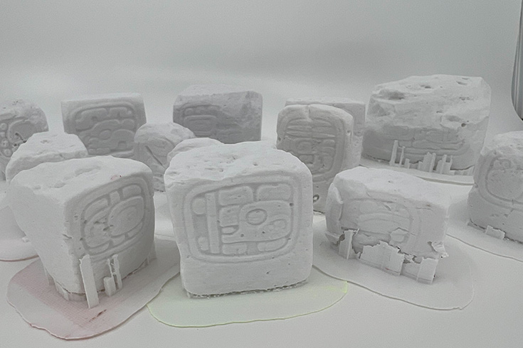 A collection of small white blocks with Mayan artwork, created on a 3D printer