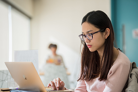 A student works on a laptop, and another student is on a laptop in the distance