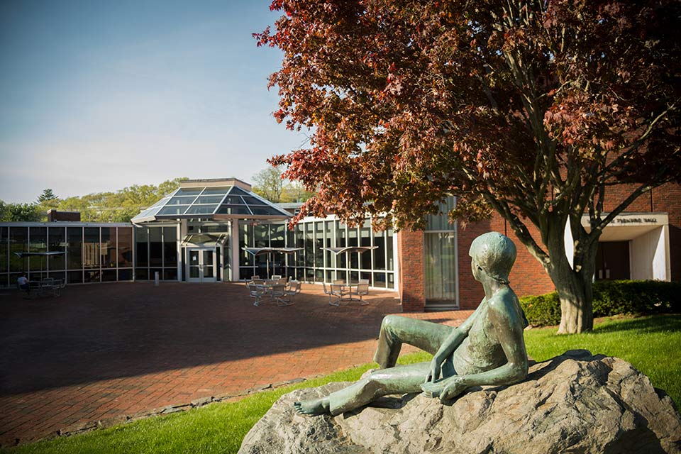 A statue in front of the Brandeis Libraries with the Goldfarb library entrance in the distance