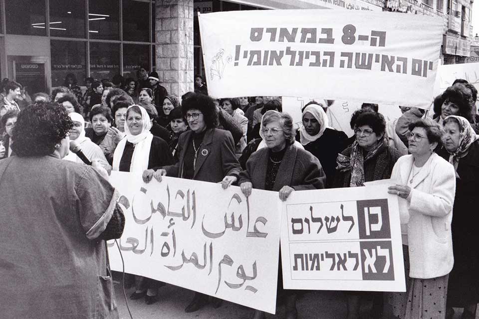 Crowd of women marching and holding signs in Hebrew and Arabic on International Women’s Day