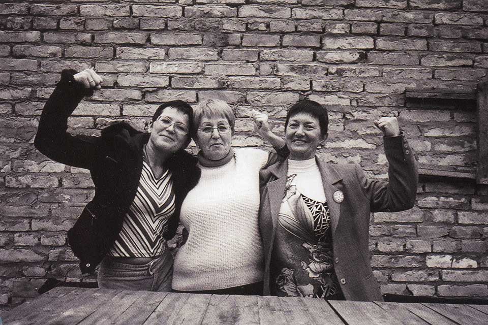 Black and white photo of three women with their arms raised.