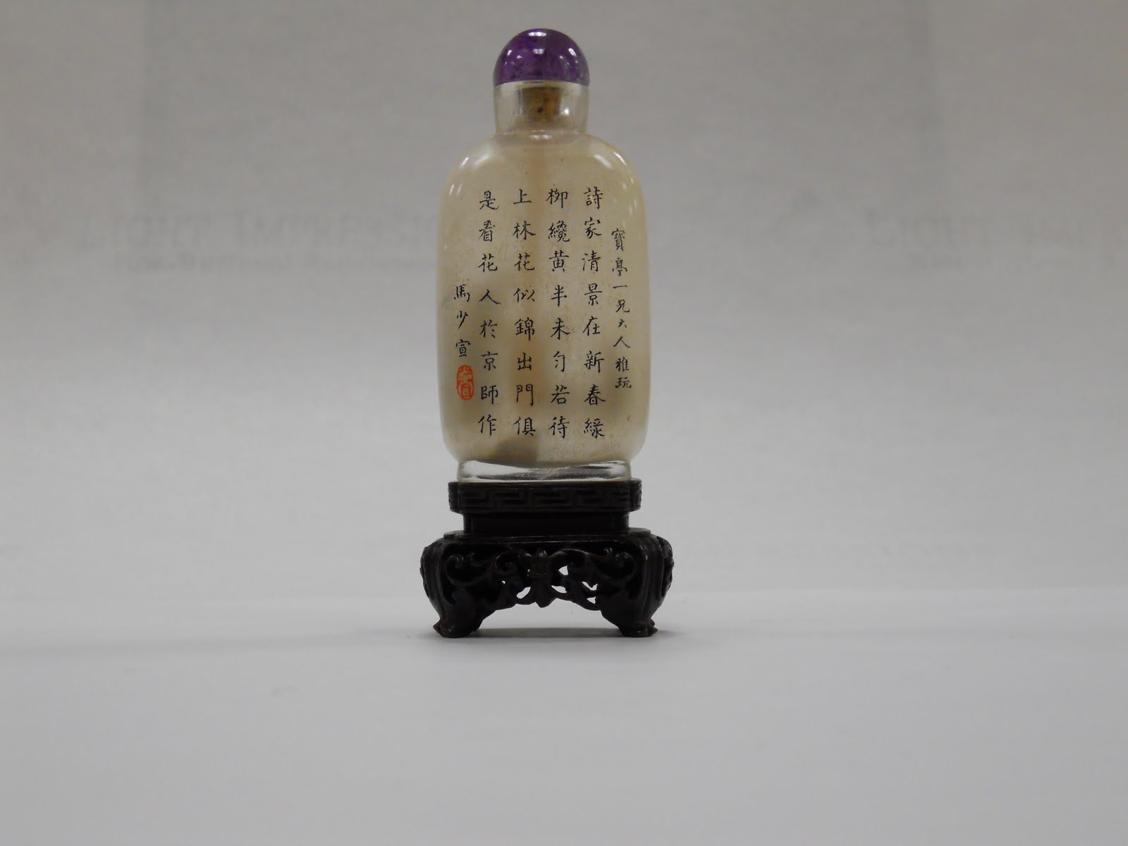 Chinese snuff bottle with black Chinese characters against a tan background and a deep purple top