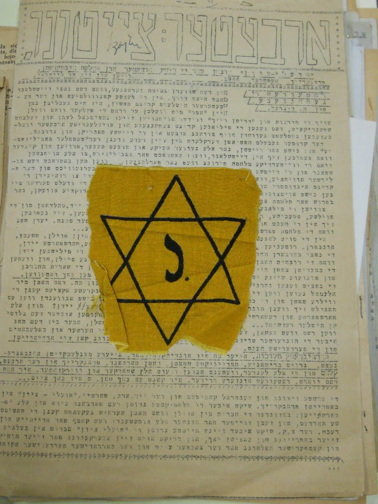 Jewish resistance newsletter written in Yiddish. A yellow fabric patch containing a Jewish star is sitting on top of the document.