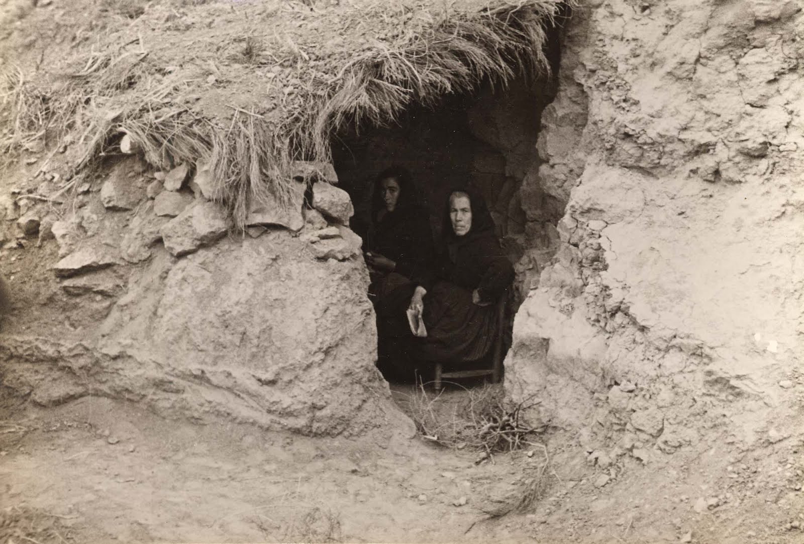 A photograph of two cloaked persons crouching inside a cave