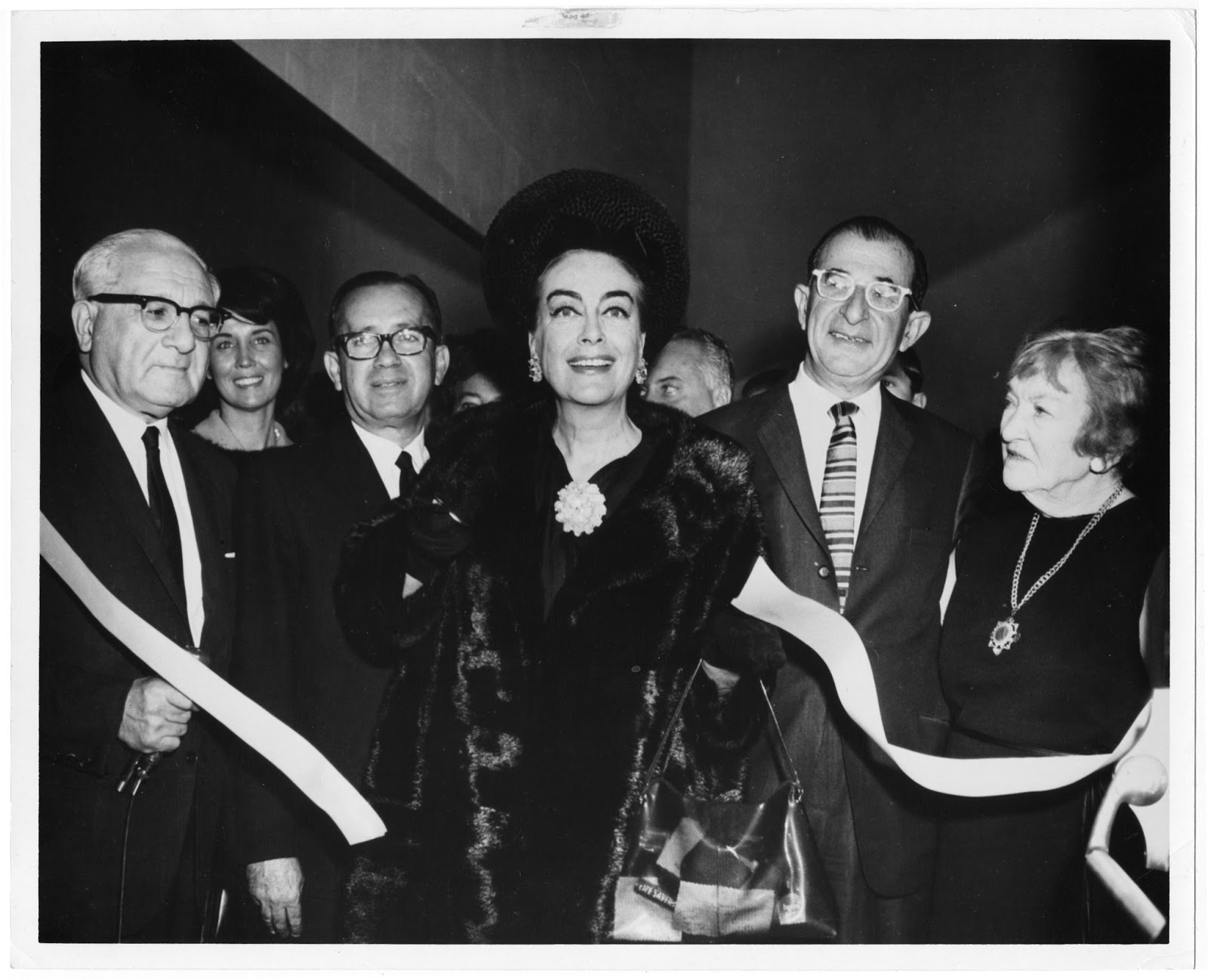 Joan Crawford, in the center of a group of people and a ribbon, opening the Joan Crawford Dance Studio in Spingold in 1965