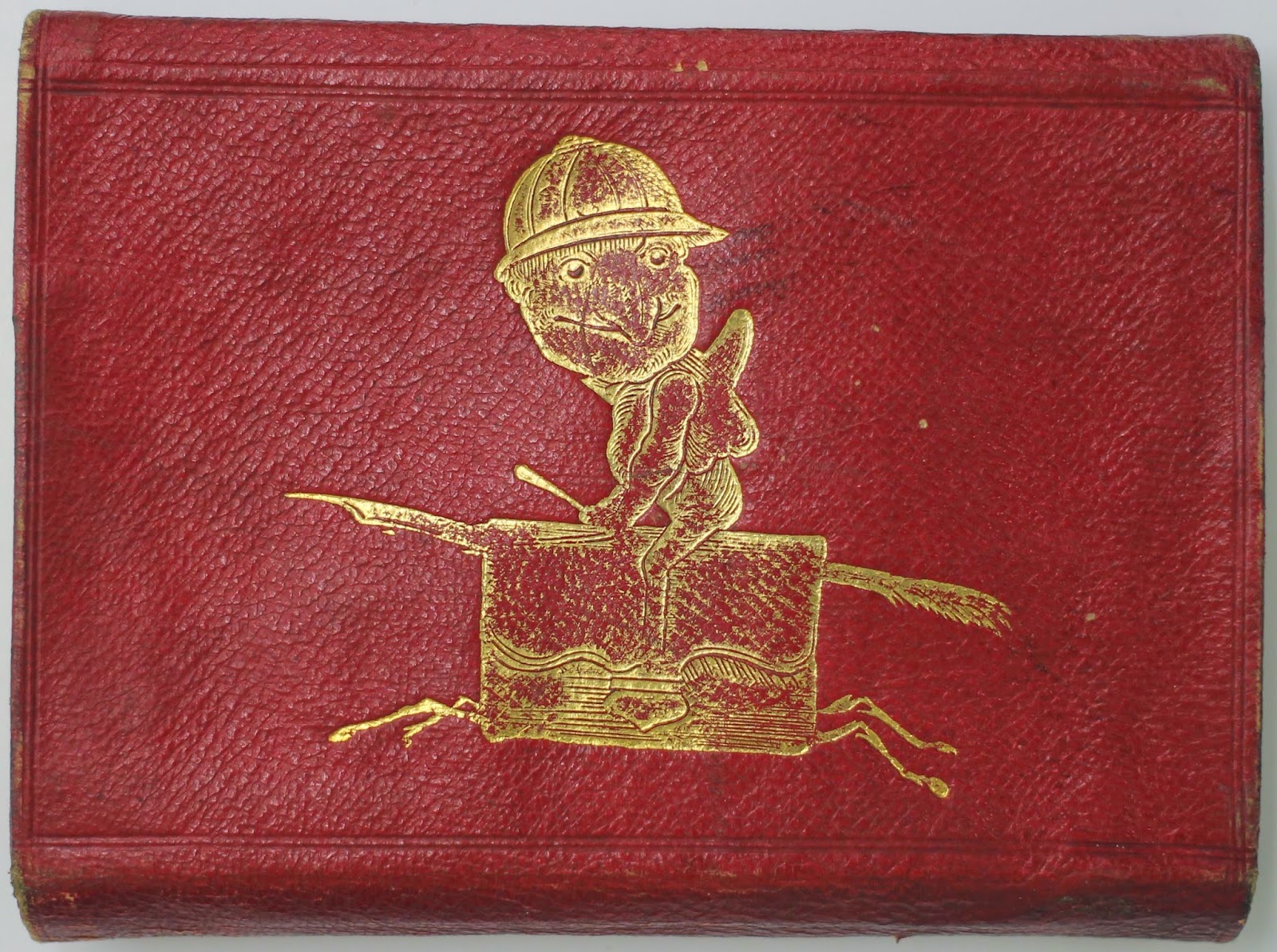 A red leather book-case with a yellow cartoon of a figure sitting on a leather-bound notebook with legs