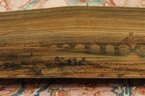 Colorfol fore-edge painting of boats, a bridge, and a group of people sitting on the shoreline