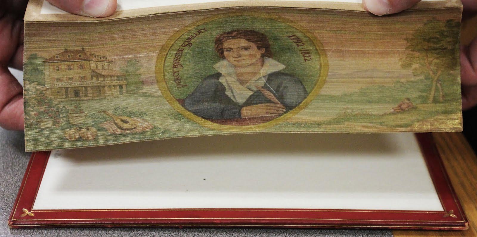 Colorful fore-edge painting of poet Percy Bysshe Shelley in the center of a quiet backyard scene with a large house, lute, and picnic blanket in view