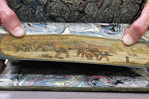 Colorful fore-edge painting of a group of men wading in water near a bridge