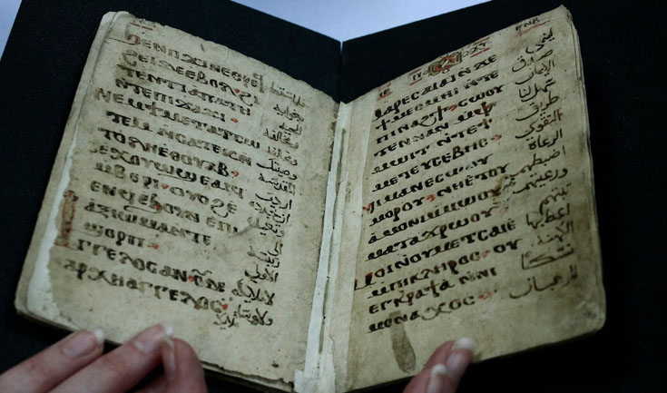 Hands holding open manuscript copy of the Anaphora of Saint Cyril. The pages of the book look very old and the writing is in black and red ink