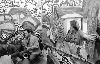 Creative Arts Festival Poetry Reading with Karen Klein and Saxophone Player Richard Ford, Artist-in-Residence April 1996. The scenery behind the performers is very animated painted line drawings of cars and other patterns.