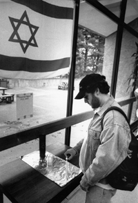 A student lighting a candle in memory of Yitzhak Rabin near an Israeli flag.