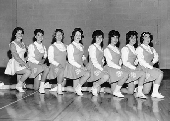 A group of cheerleaders in matching costumes pose for the camera in a row, kneeling with one knee up.