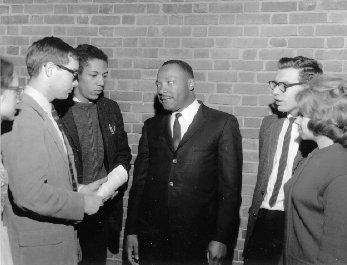 A group of students talking to Martin Luther King, Jr. They are standing in front of a brick wall.