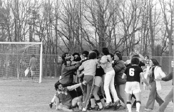 Celebrating the championship soccer game: A cluster of students hugging each other; one fell on the ground. Others approach to join in the huddle.