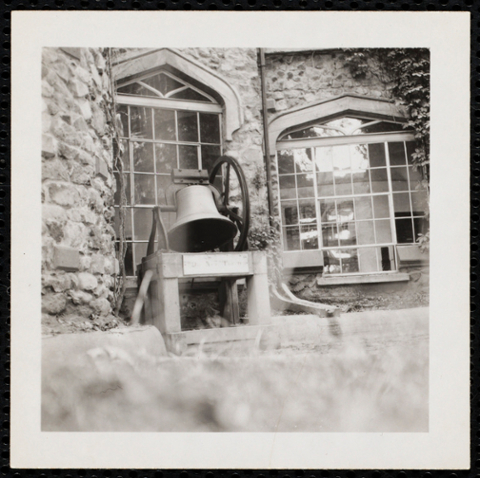 Closeup shot of bell ringing at castle with two multi-paned windows behind the bell.