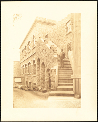 Faded photograph of a man in a suit and hat,  standing on castle stairs near a sign that reads: "Laboratories" laboratory Diagnosis Bacteriology Physics."