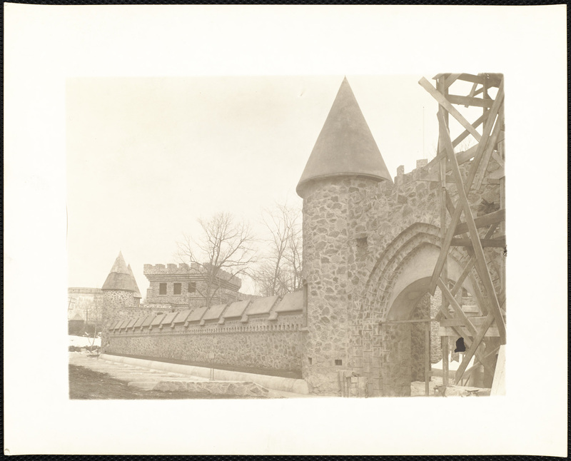 View of the stone wall and arched entryway with turret and scaffolding.