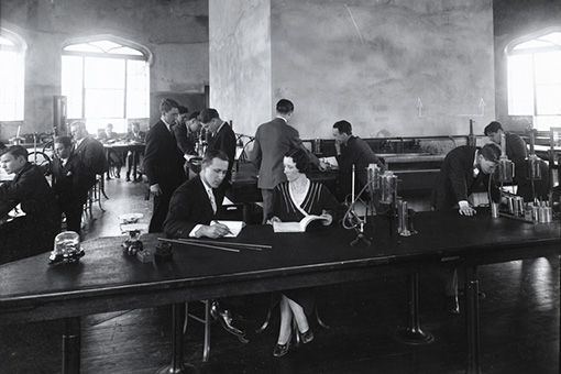 Photograph of a classroom space in the castle with a man and woman seated at the table in the front. Other students are working at tables behind them.