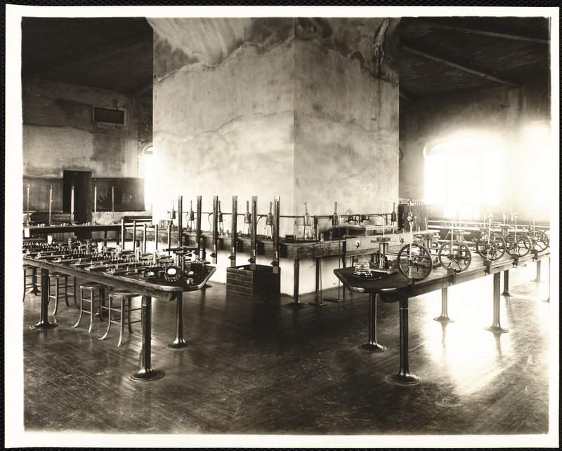 Classroom and lab. Long tables are set up with stools and equipment for each student.  One table contains small wheels. Others contain audio equipment.