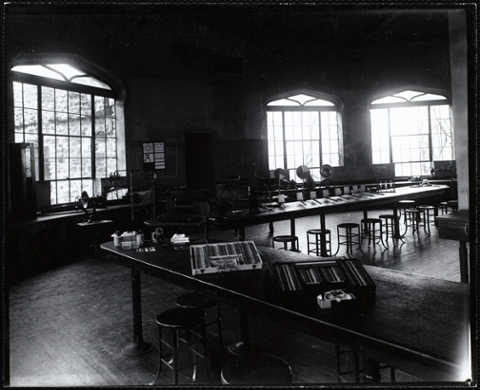 Empty lab with three large windows. A variety of lab equipment and materials are set up along the tables. An eye chart is hanging at the back wall.