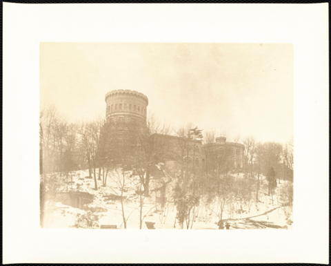 Back of castle with snow and bare trees. This photograph is faded.