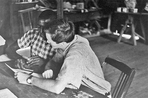 Voter education, a civil rights worker assisting an African American man, seated at a table.