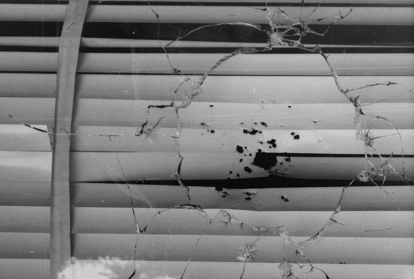 Outside window of SCOPE house after it had been shot, with shattered glass and bullet holes.