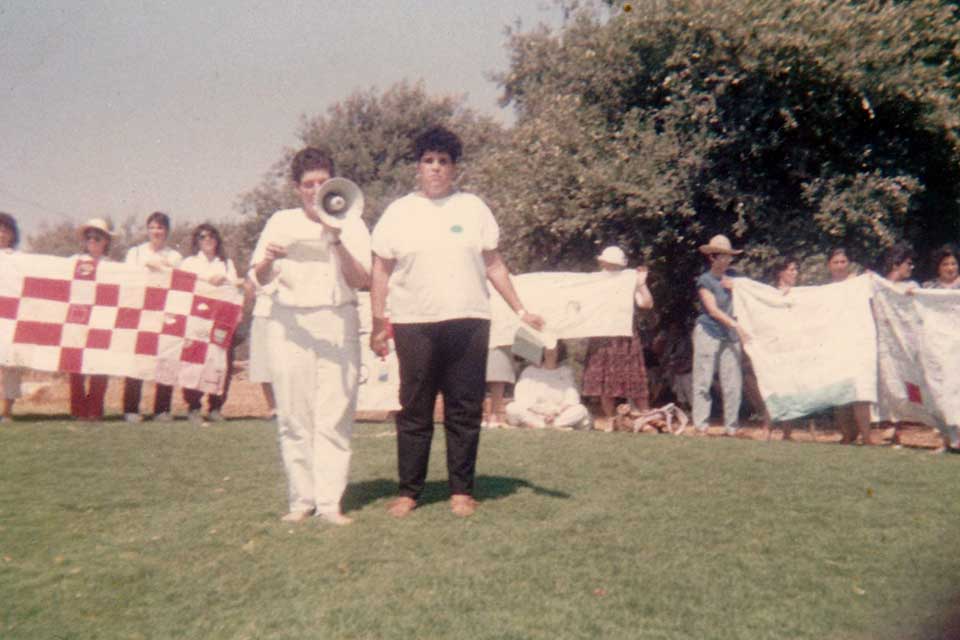 Women hold large quilt sections and speak through megaphones