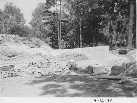 The foundation in progress. Picture shows piles of rocks and dirt, and a wheel barrow.