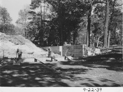 Two workers building the foundation. Portions of a wall are evident in the picture