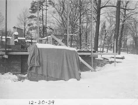 Construction site with a supplies covered by a tarp, in front of the partially built brick walls.