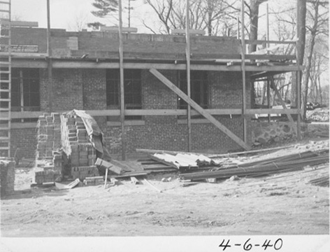 The building under construction with piles of bricks, lumber, a ladder and scaffolding.