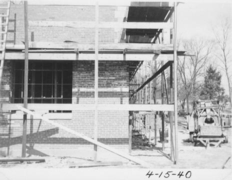 The corner of the building under scaffolding, with a construction vehicle to the side.