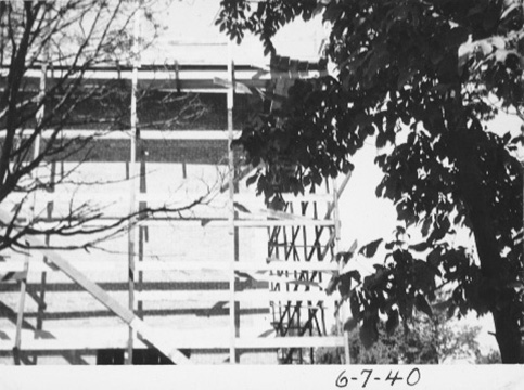Towards the end of the construction, this photo shows an upper story, with scaffolding, and trees with leaves partially obscuring the view.