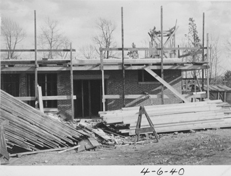 Piles of lumber in front of the building, which has scaffolding.