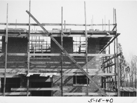 View of the corner of the building as the second story is built up behind scaffolding.