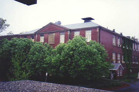 Color photo of Ford Hall, taken from the Administration Building in Summer 1999. The trees have thick green leaves.