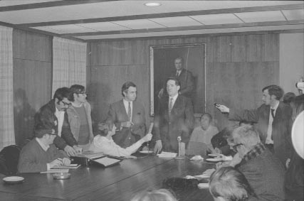 President Abram giving a press conference in a room with a long table and several reporters. Peter Diamandopoulos, Dean of the Faculty of Arts and Sciences, is to Abram's right.