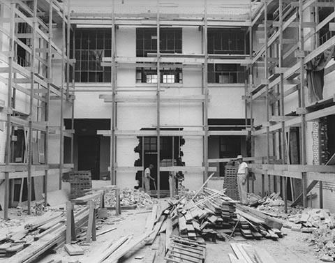Seifer Auditorium Under Construction, with piles of lumber and debris, a hole in a wall of the attached building and 3 construction workers.