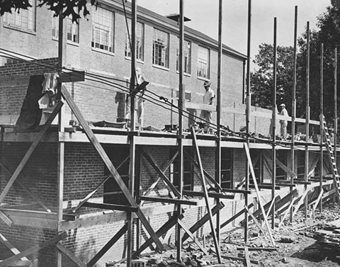 Three workers standing on scaffolding during the construction of Sydeman Hall.