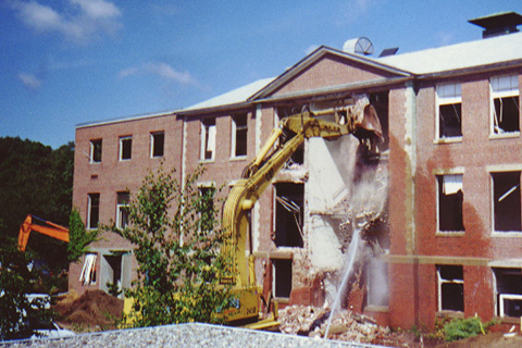 Wrecking crew tearing down the building with crane and hoses spraying.